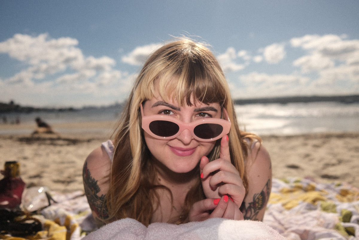 Woman sat on beach looking at the sea with a upper back tattoo and black bikini